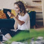 A young woman applying makeup in a bright room.